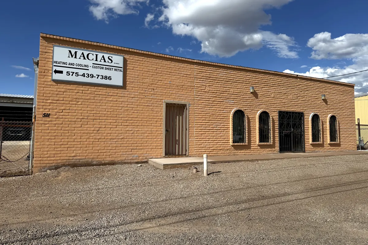 The Macias Heating and Cooling shop in Alamogordo, New Mexico: a long brick building under a deep blue sky, with a sign reading Macias, Heating and Cooling, Custom Sheet Metal.