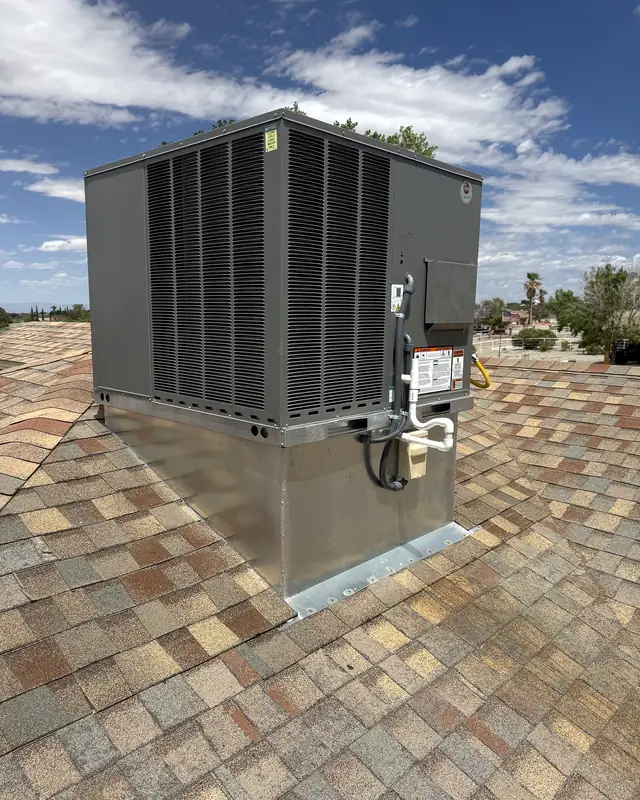 A new dark grey packaged rooftop unit set on a galvanized sheet-metal curb on the same shingled roof.
