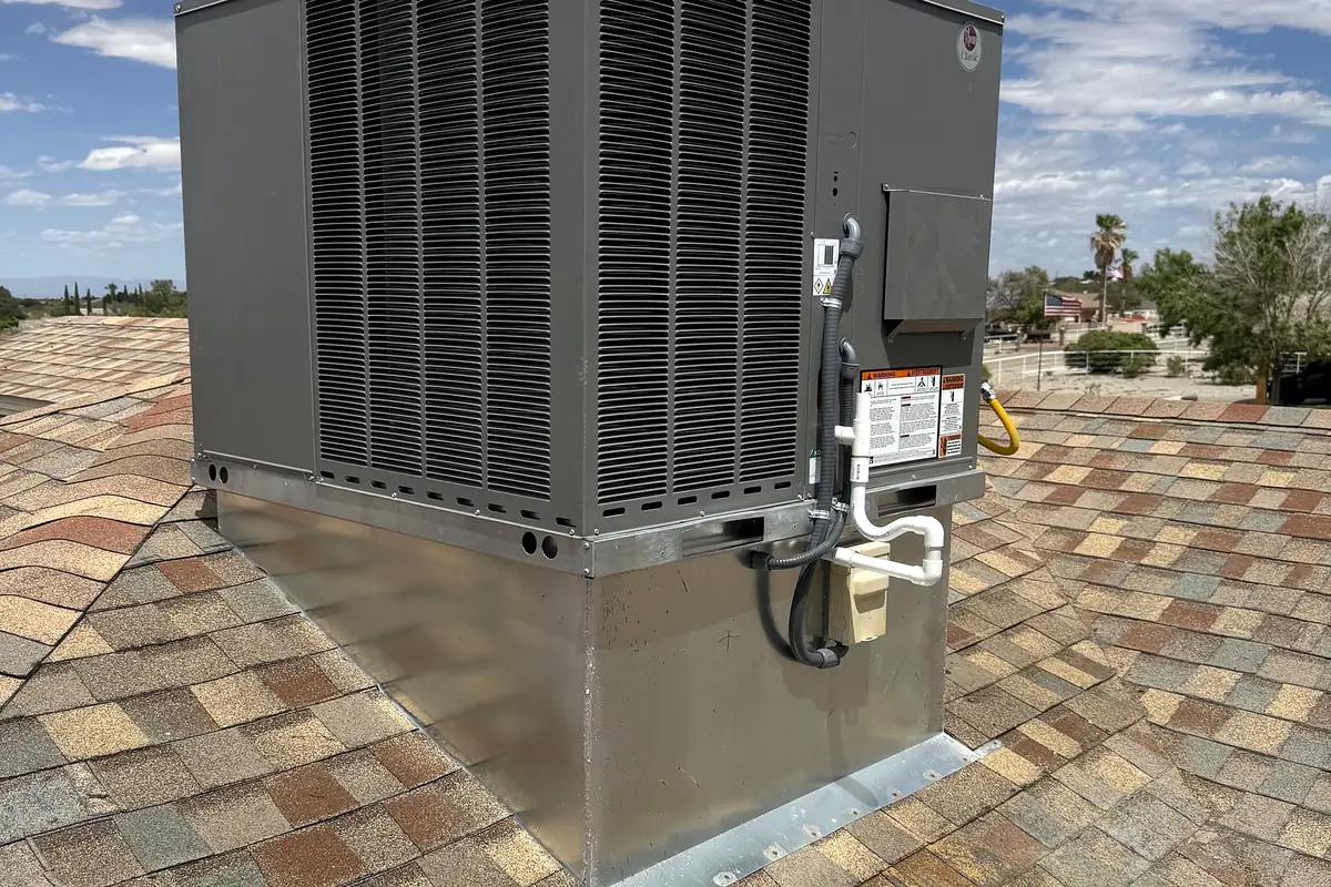 A new dark grey packaged rooftop unit on a galvanized sheet-metal curb on a shingled house roof.