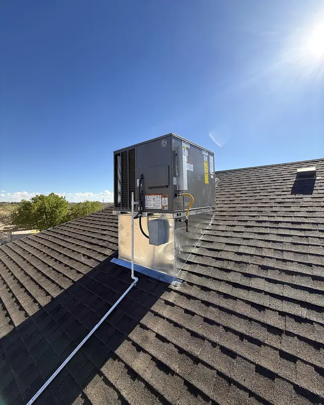 The new packaged rooftop unit on a galvanized curb on the same dark shingled roof, under a clear sky.