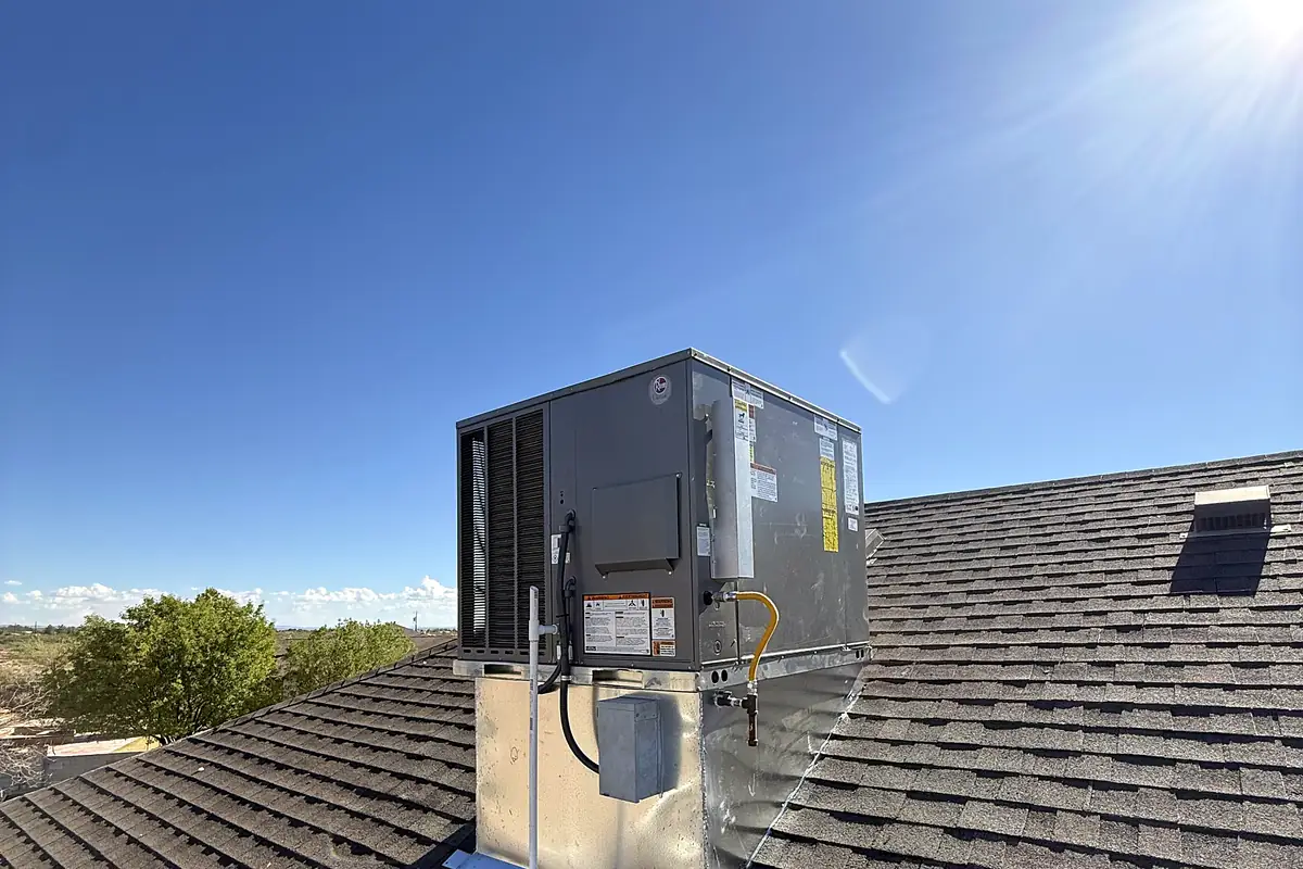 A new packaged rooftop unit on a galvanized curb on a dark shingled roof under a clear sky.