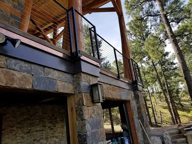 Custom copper trim under the deck of a stone and timber cabin among the pines.