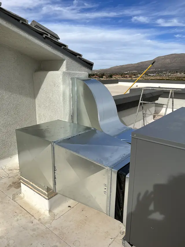 Galvanized duct with offsets running from a packaged unit into the wall of a house.