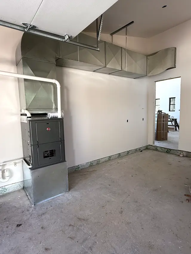 A new furnace and its galvanized duct in an unfinished room of a new build.