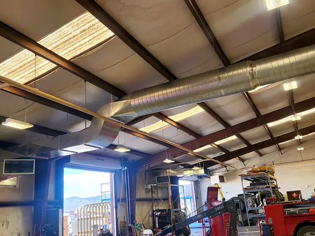 Another view of spiral duct in a large vehicle shop, bay door open.