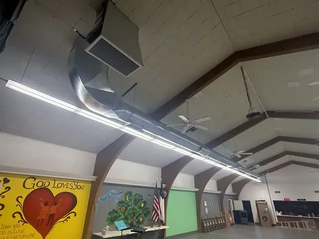 Exposed spiral duct with a radius elbow up to a supply grille in a large community hall.