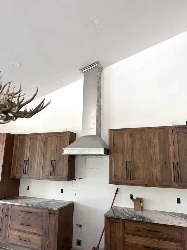 A range hood with a metal chimney cover running up to a vaulted ceiling, between wood cabinets.
