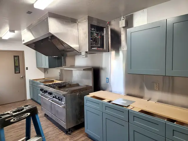 A stainless commercial kitchen hood installed over a range, with new cabinets going in.