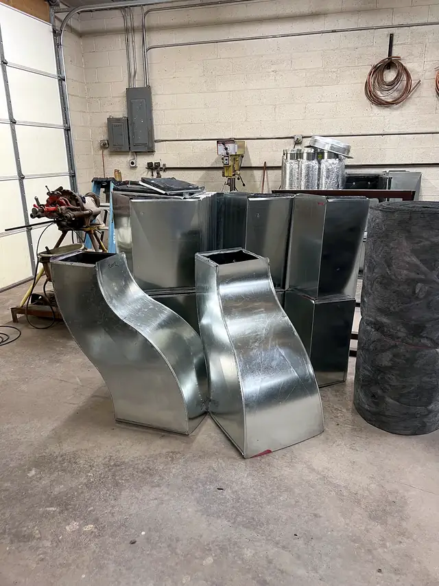 Several galvanized offsets and transitions grouped on the shop floor.