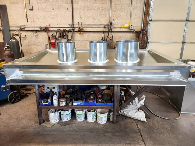 A custom galvanized chimney cap for a fireplace, with three round flue collars, on the shop bench.