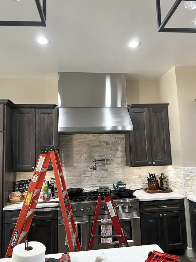 A brushed stainless range hood over a professional range in a home kitchen.
