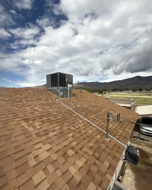 A finished rooftop unit on a tan shingled roof, with mountains and a cloudy sky behind.