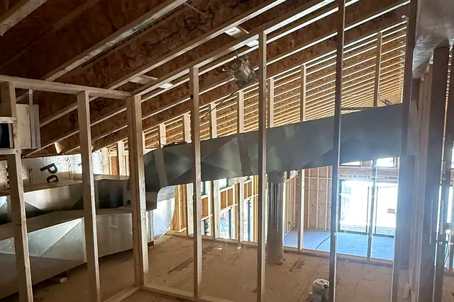 A galvanized main duct trunk running through the framing of a building under construction.