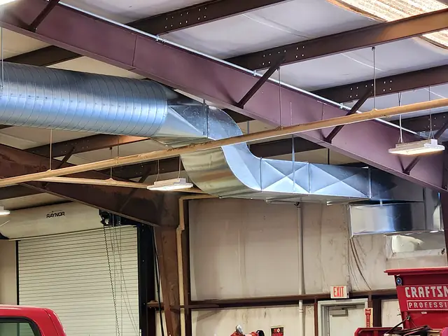 Spiral duct with rectangular drops under a steel-beamed ceiling in a large workshop.