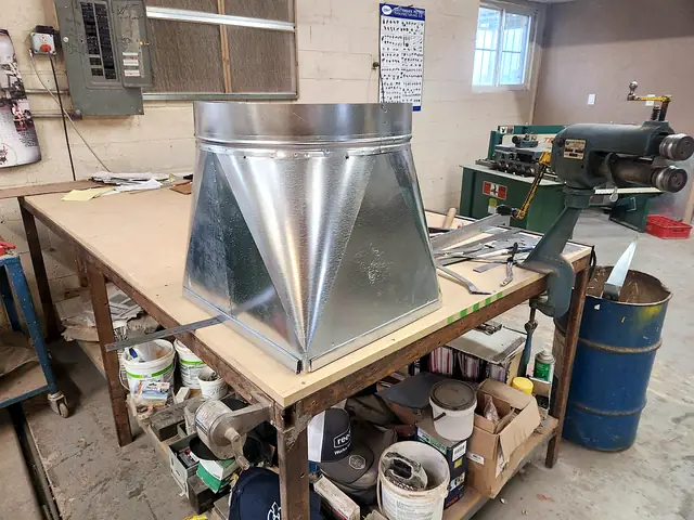 A large galvanized square-to-round transition on a workbench.