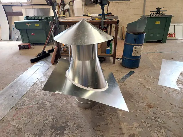 A round roof vent with a cone rain cap and a flat flashing base, on the shop floor.